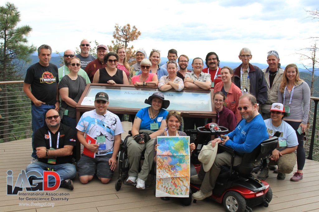 Field trip participants gather around an interpretive sign at an overlook in Arizona with rolling blue hills and pine trees in the background.