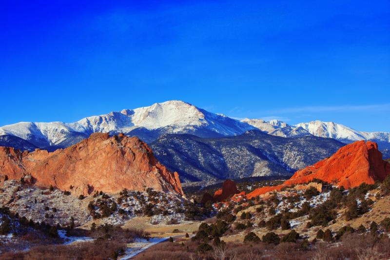 Snow-covered Pikes Peak rises in the distance behind the giant vertical red slabs of rock at Garden of the Gods