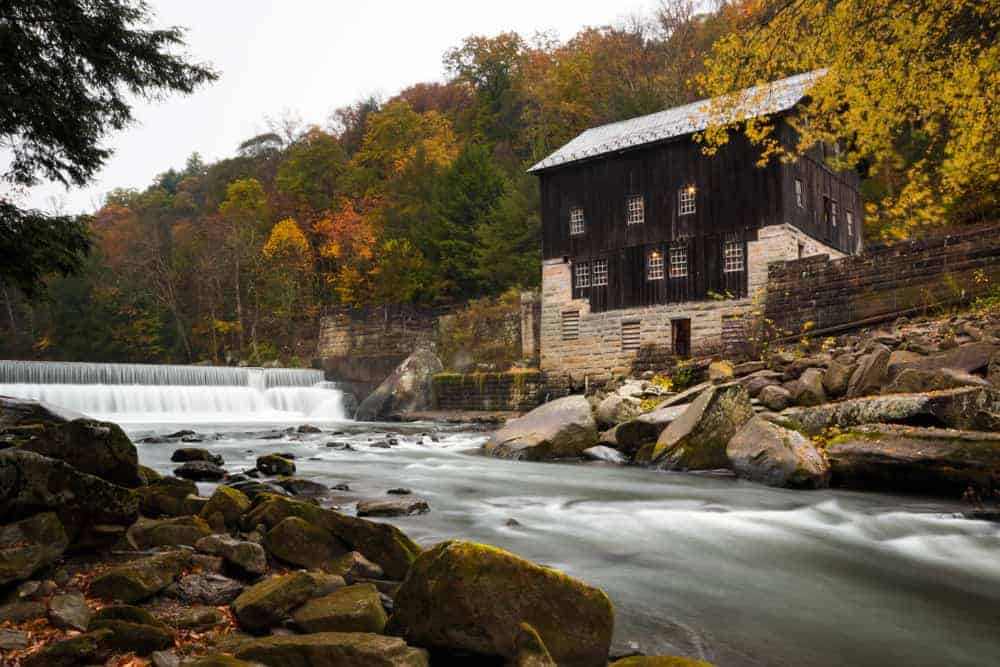 A river with a spillway cascades by a old multi-story millhouse.