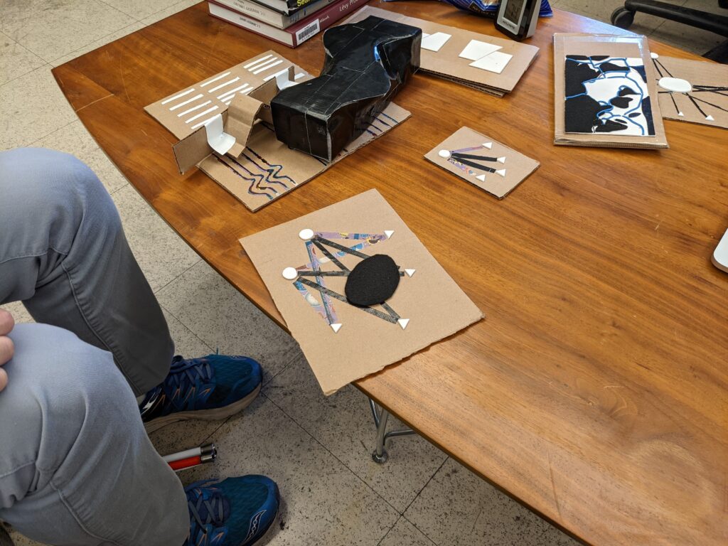 A photo showing a table covered with various tactile diagrams. These objects are made of materials like foam, felt, and cardboard.