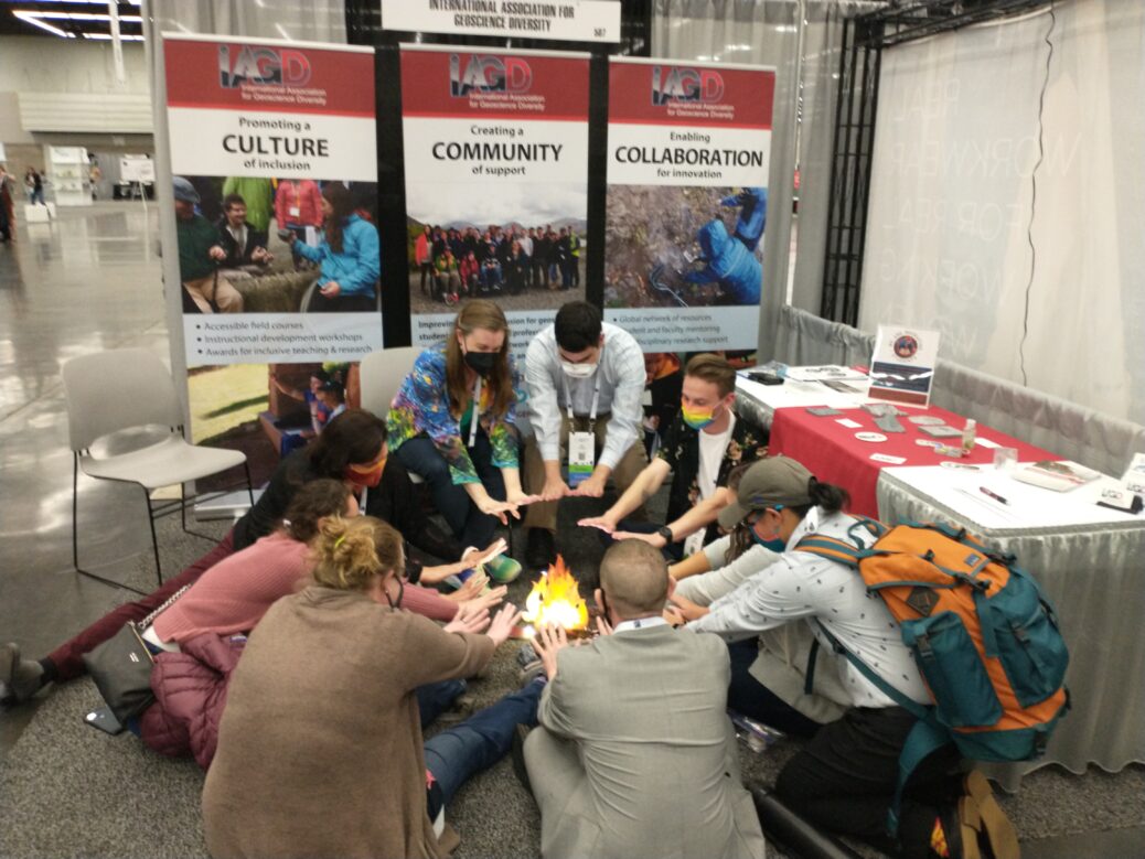 visitors to the IAGD booth at GSA conference huddle around a cardboard fire and pretend to warm their hands.